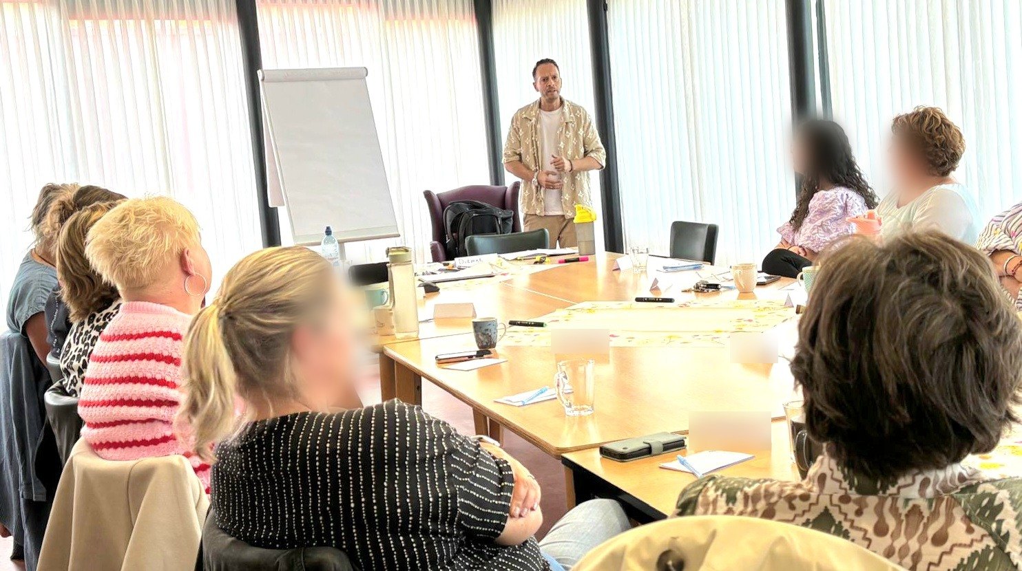 Trainer staat voor een groep deelnemers rond een tafel tijdens een training
